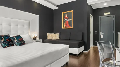 Camera d'albergo moderna con letto bianco, divano nero e pavimento in legno