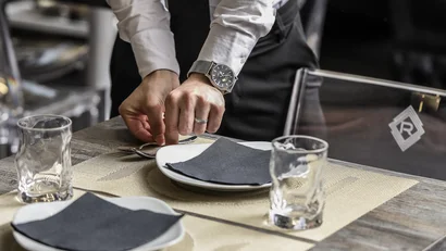 Mani che sistemano posate su una tavola apparecchiata in un ristorante.