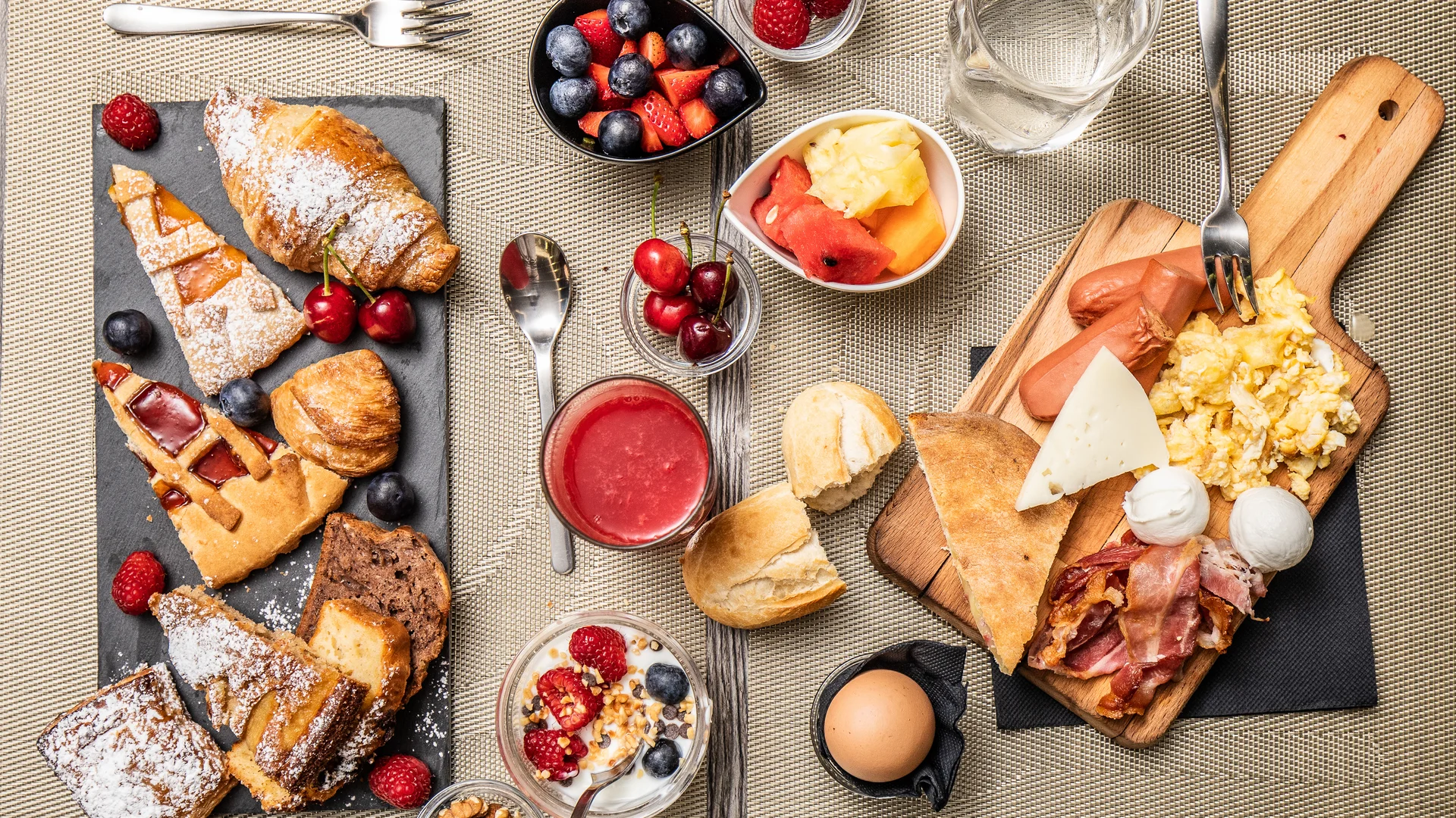 Colazione con dolci, frutta fresca, uova strapazzate, bacon e pane