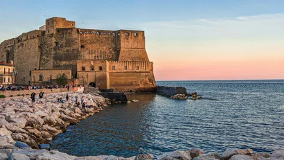 Castello a Napoli sul mare con scogli e cielo al tramonto