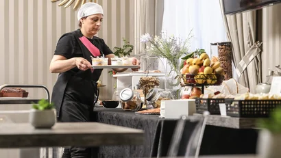 Donna con berretto da cucina che sistema dessert su un tavolo con frutta e dolci