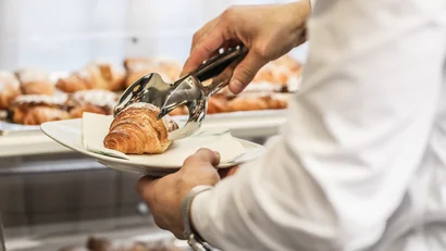 Persona che prende un croissant con pinze in una pasticceria
